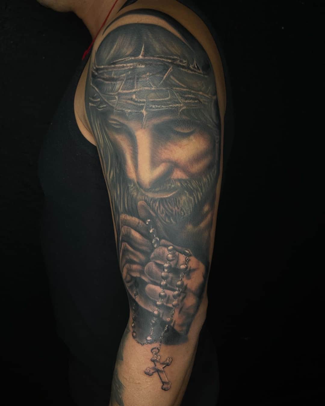 Praying hands, jesus and cross tattoo on the upper arm, half sleeve, Chicano style, by Inksane Shorty in Austin, TX