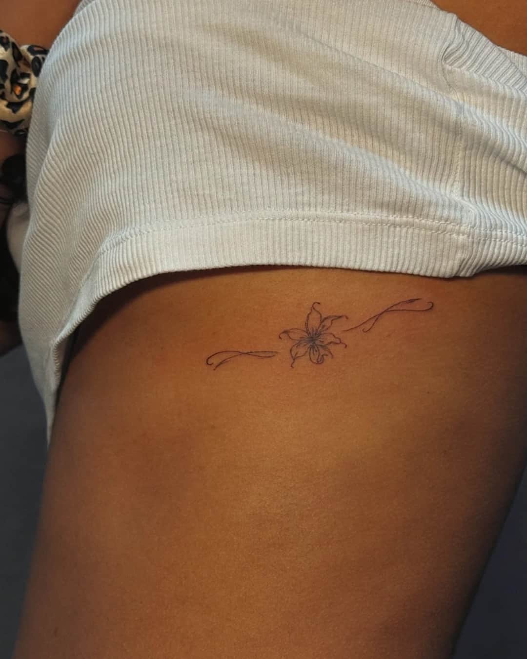 Small flower tattoo on the thigh, Fine Line style, by Luisa Duarte in Austin, TX
