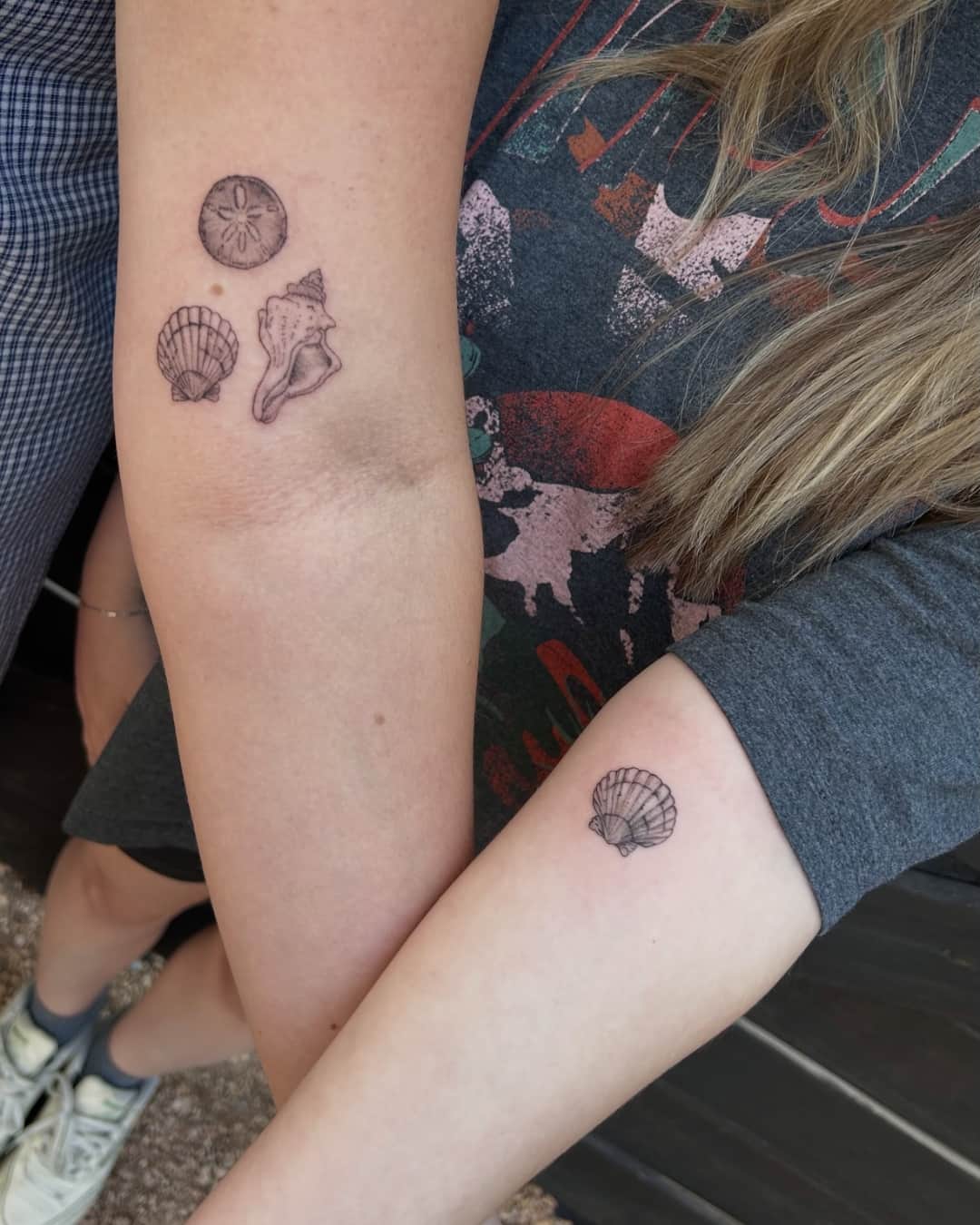 Small seashell, scallop shell and sand dollar tattoo on the upper arm, Fine Line style, by Slowpoke Tattoo - Salina in Austin, TX