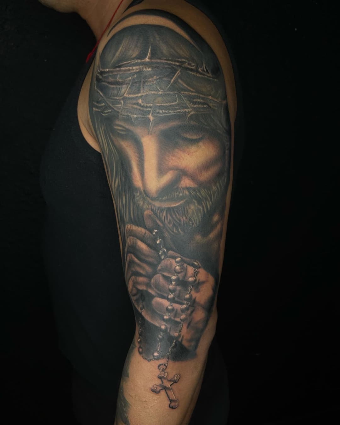 Praying hands, jesus and cross tattoo on the upper arm, half sleeve, Chicano style, by Inksane Shorty in Austin, TX
